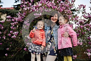 Happy Mother\'s Day. Mother with two daughters enjoying nice spring day near magnolia blooming tree