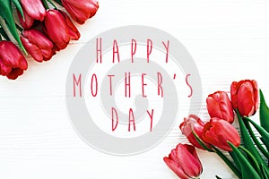 Happy Mother`s Day text and beautiful red tulips on white wooden background flat lay. Happy mother day greeting card with spring