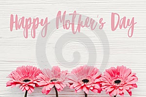 Happy Mother`s Day text sign at pink gerbera on white wooden background, flat lay. Floral greeting card. Mothers day. Pink