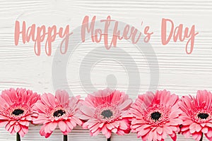 Happy Mother`s Day text sign at pink gerbera on white wooden background, flat lay. Floral greeting card. Mothers day. Pink