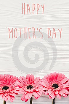 Happy Mother`s Day text sign at pink gerbera on white wooden background, flat lay. Floral greeting card. Mothers day. Pink