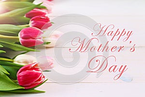 happy mother's day text sign on pink tulips on white rustic wooden background. greeting card concept. sensual tender women image.
