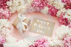 Happy Mother`s Day text sign on pink and white peonies with gift box and card on pastel pink paper. Stylish greeting card