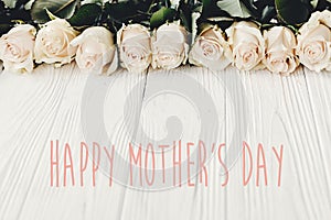 Happy Mother`s Day text sign at white roses on wooden background. Floral greeting card. Stylish border of white flowers. Mothers