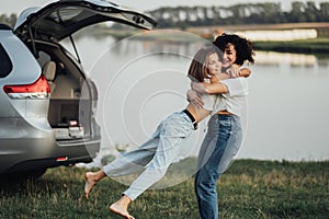 Happy Mother's Day, Woman Hugging with Cheerful Teenage Daughter Outdoors on Background of Car and Lake