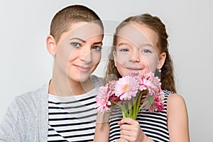 Happy Mother`s Day, Women`s day or Birthday background. Cute little girl giving mom, cancer survivor, bouquet of pink daisies.