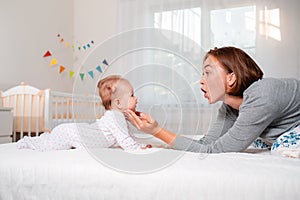 Happy Mother`s Day. A young mother plays with her baby on the bed. Side view. The concept of motherhood