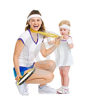 Happy mother showing baby medal for achievements in tennis