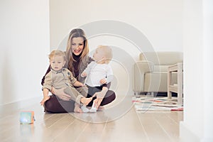 Happy mother sitting on the floor with her two babies and playing