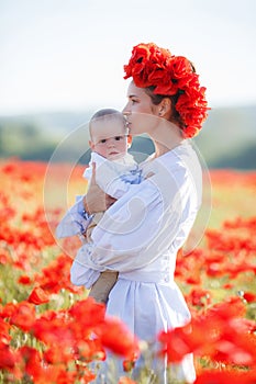 A happy mother with a small son in her arms on the endless field of red poppies on a sunny summer day
