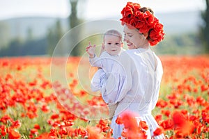 A happy mother with a small son in her arms on the endless field of red poppies on a sunny summer day