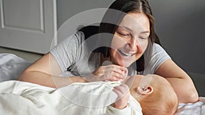 Happy mother smiles playing with little baby sitting at bed