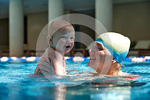 Happy mother, smiling, holding cute with little kid, girl, daughter in swimming pool indoors on warm sunny day