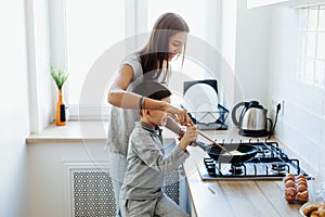 Happy mother with son cooking omelet in kitchen at home