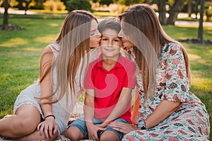 Happy mother, son and daughter in the park. Mom and sister kiss their son. Happy family concept