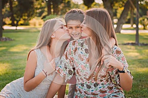 Happy mother, son and daughter in the park. Mom and sister kiss their son. Happy family concept.