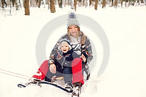 Happy mother and son having fun with sledge in a park. Winter snowy day. Lovely toddler boy with his mom on a sled. Winter