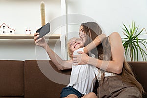 Happy mother and son hugging and take selfie on smartphone. Home leisure