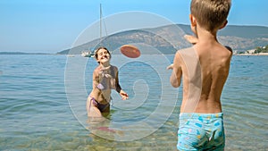 Happy mother with son playing frisbee on the sea beach. Family holiday, vacation and fun summertime of children and