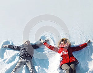 Happy mother and son playing having fun together lying in snow winter