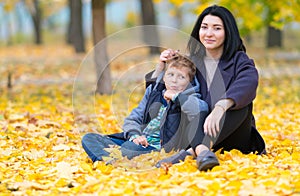 Happy mother and son sitting in yellow fall leaves.