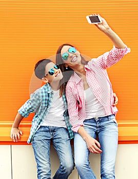 Happy mother and son teenager taking picture self portrait on smartphone in city