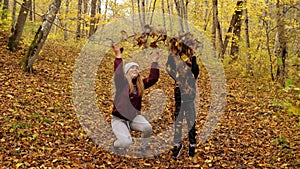 Happy mother and son toss yellow fallen leaves in the autumn forest.