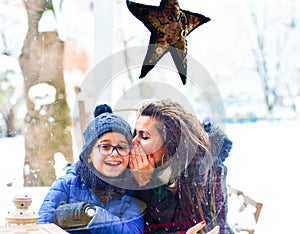 Happy mother  and son whispers  sitting outdoor at winter christmas time.  Family fun. Christmas card