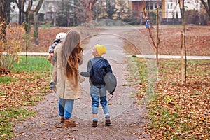 Happy mother and sons going to school and to kindergarten. Mother with two sons on walk in autumn. Back to school. Happy family in