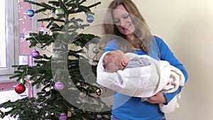 Happy mother sway newborn baby in hands near Christmas tree