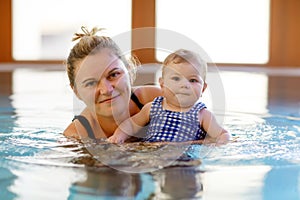 Happy mother swimming with cute adorable baby daughter in swimming pool. Smiling woman and little child, girl of 6