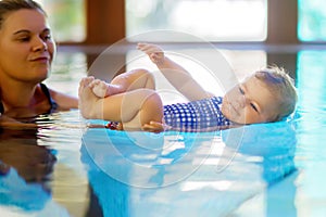 Happy mother swimming with cute adorable baby girl daughter in swimming pool spending spa vacations