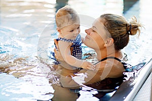 Happy mother swimming with cute adorable baby girl daughter in swimming pool spending spa vacations