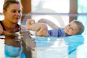 Happy mother swimming with cute adorable baby girl daughter in swimming pool spending spa vacations