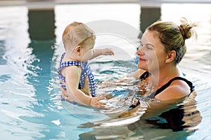 Happy mother swimming with cute adorable baby girl daughter in swimming pool spending spa vacations