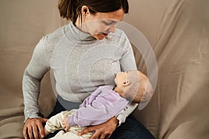 Happy mother taking care of her small baby sleeping in her arms at home