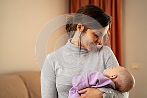 Happy mother taking care of her small baby sleeping in her arms at home