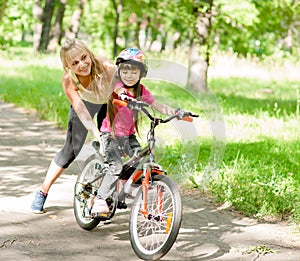 Happy mother teaches his daughter to ride a bike