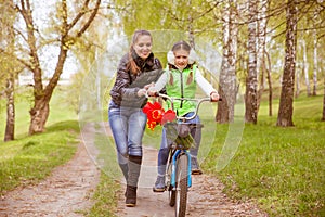 Happy mother teaches his daughter to ride a bike. Mother holds daughter from falling