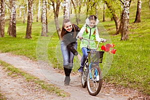 Happy mother teaches his daughter to ride a bike in the park