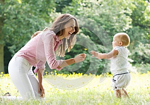 Happy mother teaching baby to walk in the park