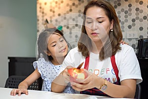 happy Mother teaching daughter peeling red apples together on table in kitchen at home . loving family.  child girl excited