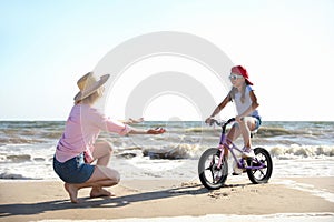 Happy mother teaching daughter to ride bicycle on sandy beach near sea