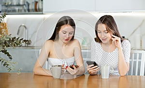 Happy mother and teen daughter looking at their phones sitting at kitchen table