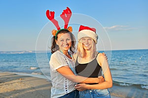 Happy mother and teen daughter in Santa Claus hat on beach, New Year Christmas holidays