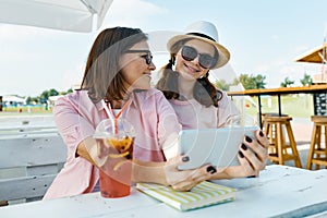 Happy mother and teen daughter talking and smiling. Parent with child in summer outdoor cafe enjoying a cold drink on a hot summer