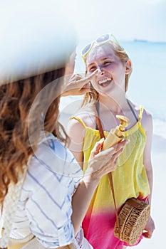 Happy mother and teenage daughter at beach applying sunscreen