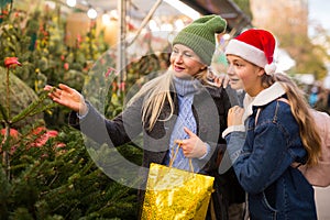 Happy mother and teenage daughter looking for Christmas tree on outdoor market