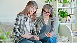 Happy mother and teenage daughter looking together at screen of digital tablet