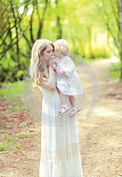 Happy mother tenderly kissing her baby holding on hands in spring